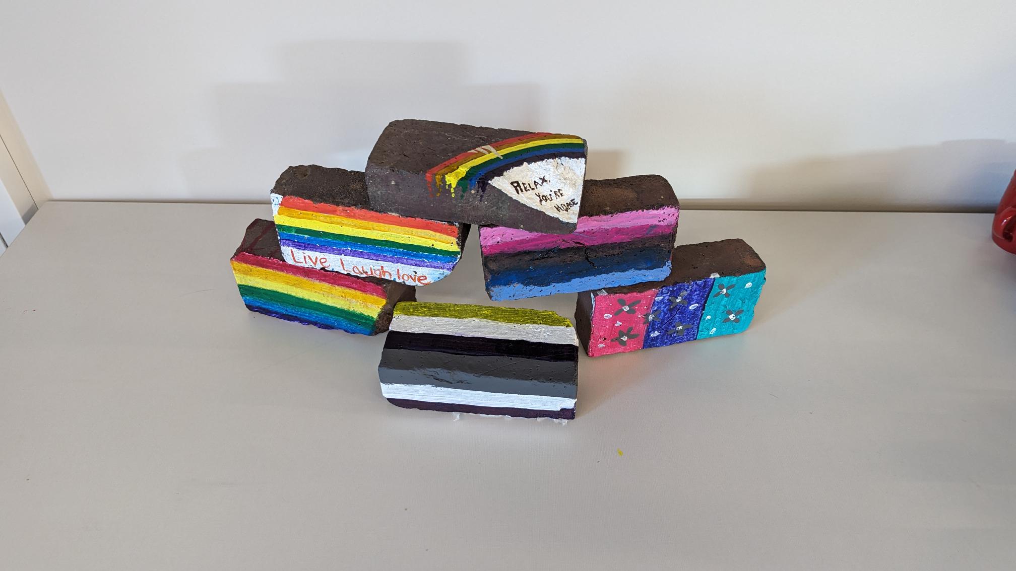 stack of bricks painted with various LGBTQ+ flags and rainbow imagery 