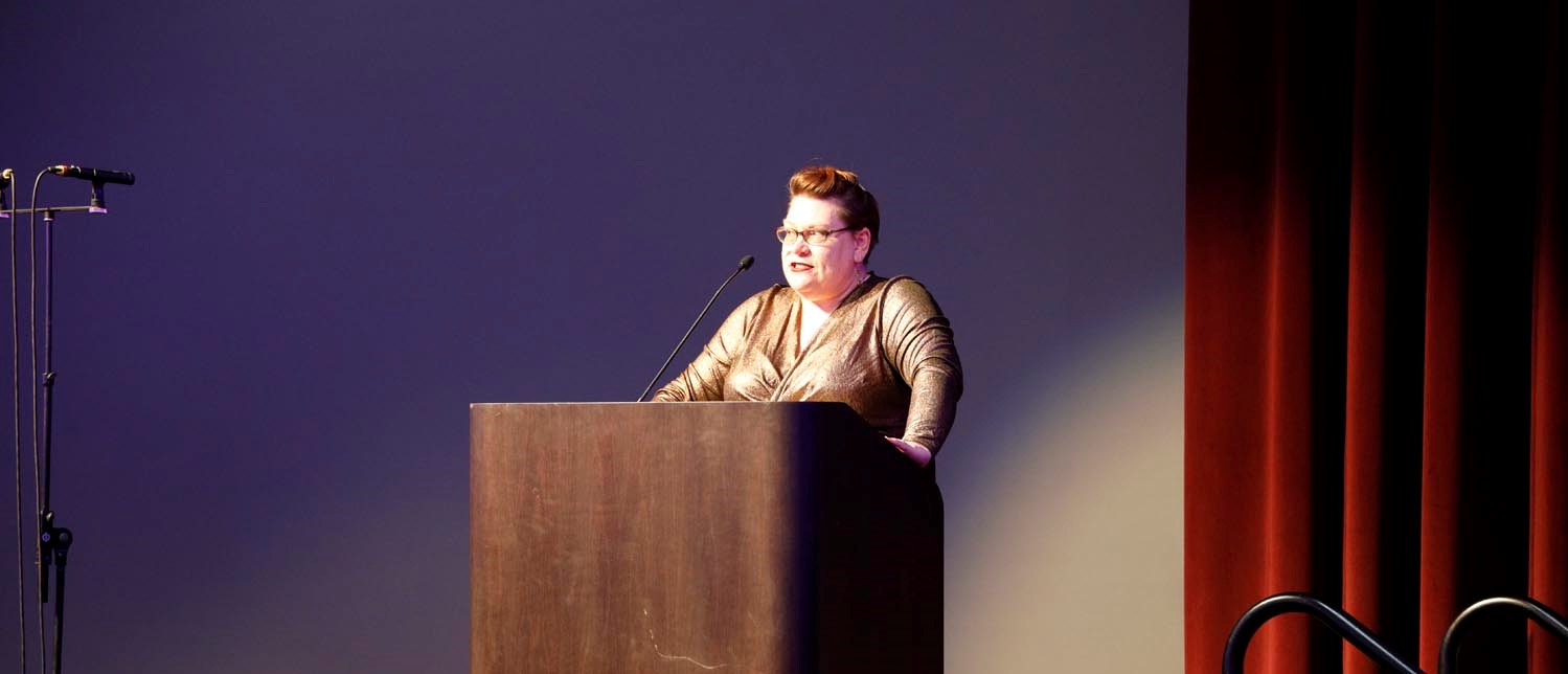Dr. Sue speaking at a podium at the Gayla